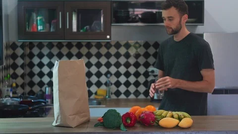 Attractive Man Drinking Water in Kitchen near Vegetables and Fruits Stock Footage 114669840