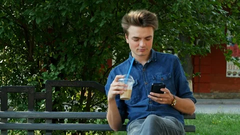 An attractive man drinks a cold cocktail and uses a mobile phone on a bench Stock Footage 113229588