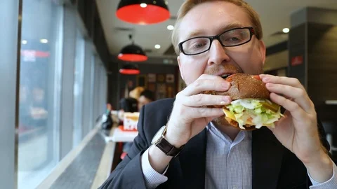 Attractive man with glasses eating Burger in fast food cafe. Slow motion Stock Footage