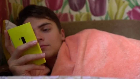 Attractive man at home lying in bad and using smartphone Stock Footage 70145096