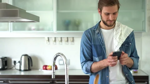 Attractive man at home using smartphone in kitchen sending message Stock Footage 159553386