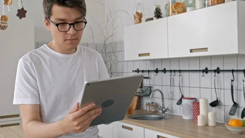 Attractive man at home using tablet in kitchen sending message on social media Stock Footage 97658867