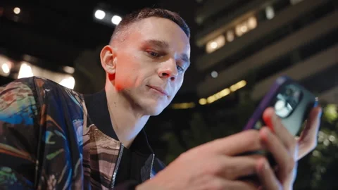 An attractive man in a jacket is using his cell phone outside at nighttime Stock Footage 259458817