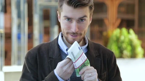 Attractive man leafing through a bundle of euros, looking at camera and smiling Stock-Footage 68401832