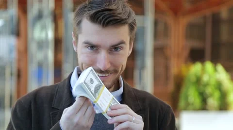 Attractive man leafing through a bundle of dollars and smelling cash Stock-Footage 68401894