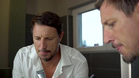 An attractive man looking himself in the mirror while shaving his beard. 4K 스톡 동영상 139885739