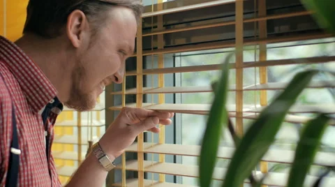 Attractive man looking through the blinds of the window to the street Stock Footage 49336260