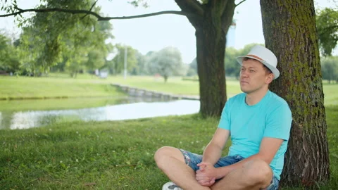 Attractive man resting while sitting under a tree, tracking by camera Stock Footage 138962649
