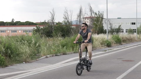Attractive Man rides his foldable electric bike on the street and smiles Video stock 131406278