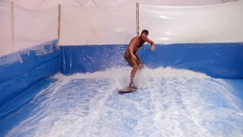 Attractive Man riding surf board on wave simulator indoors. Young surfer during Stock Footage 212362576