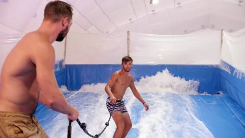 Attractive Man riding surf board on wave simulator indoors. Young surfer during Stock Footage 212363581