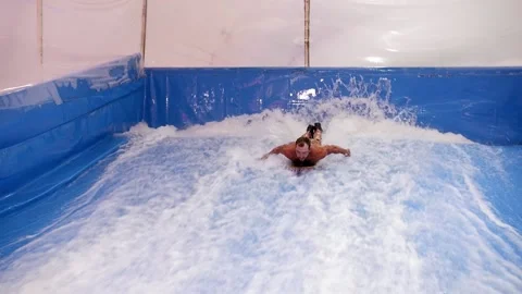 Attractive Man riding surf board on wave simulator indoors. Young surfer during Stock Footage 212364019