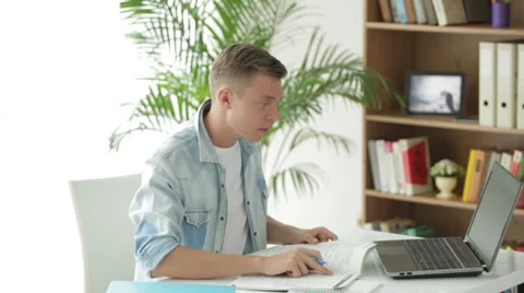 Attractive man sitting at table using laptop and writing in notebook Stock Footage 27692031