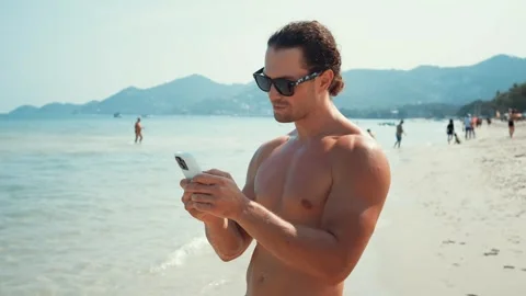 Attractive man stands on beach using phone chat with friends modern technology Stock Footage 273952096