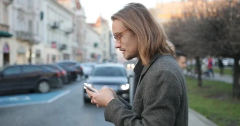Attractive man in stylish clothes strolling through the city uses a smartphone Stock Footage 127397615