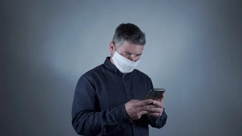Attractive man with types of protective mask on the smartphone on a gray back Stock Footage 129420693