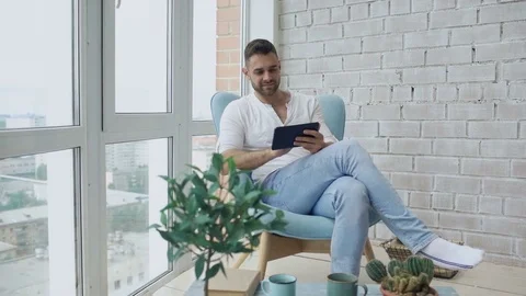 Attractive man using digital tablet sitting in chair at balcony in loft modern Stock Footage