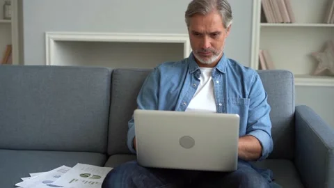 Attractive man using his laptop sitting at home on the sofa in the living room Stock Footage 139745906