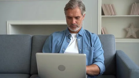 Attractive man using his laptop sitting at home on the sofa in the living room Stock Footage 139745912