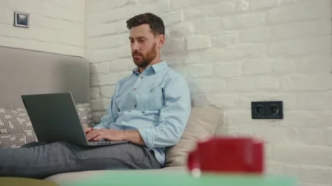Attractive man using laptop typing working lying on couch in modern living room Stock Footage 132539804