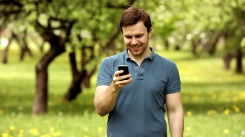 Attractive man using mobile phone in park at the green background Stock Footage 63194915