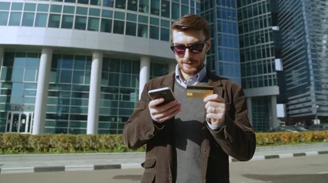 Attractive man using online banking on smartphone with credit card in the street Video stock 68398163