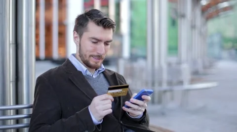 Attractive man using online banking on smartphone with credit card in the street Stock Footage 68401882