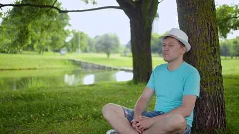 Attractive man in white hat resting on the grass under the tree Stock Footage 141811072