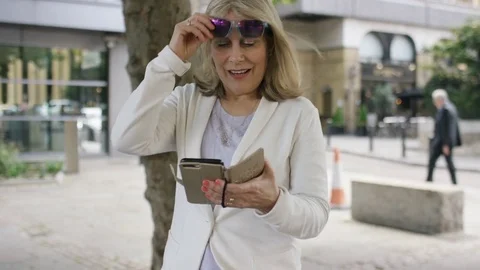 Attractive mature woman in shades walks and uses her phone, in slow motion Stock Footage