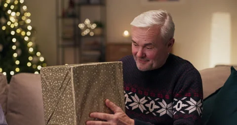 Attractive middle-aged man with gray hair sitting on the couch holding present Stock Footage 210594124