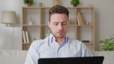 Attractive millennial guy sit on sofa in living room work from home use laptop Stock Footage 169017909