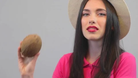 Attractive model shows a coconut. Pink polo and hat on a white background Stock Footage 73569080