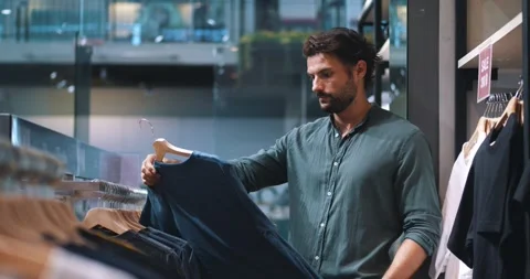 Attractive multi-ethnic dark-haired bearded young man, inspecting casual shirts Stock Footage 219274466