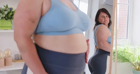 Attractive obese woman posing in front of mirror at home, chubby overweight plus Stock-Footage 313344154