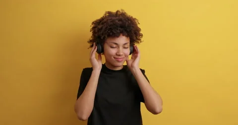 Attractive pleased dark skinned young woman keeps eyes closed wears headphones Stock Footage 150298556
