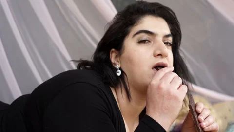 Attractive plus size model lying on bed eating chocolate Stock Footage 106069383