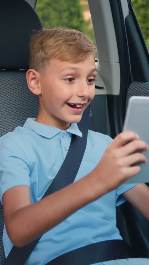 Attractive positive blond 10-year-old boy fastened by safety belt on backseat of Stock Footage 329435156
