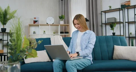 Attractive positive satisfied young blond haired girl sitting on soft couch in Stock Footage 149690340