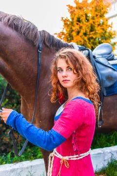Attractive pretty red-haired, long-haired young girl stands half-ass and looks a Stock Photos