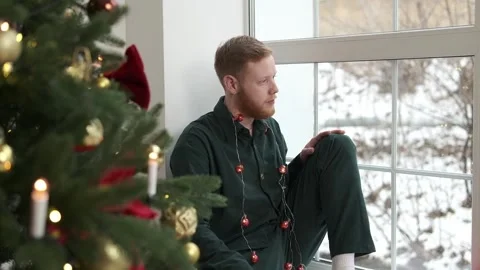An attractive red-haired, bearded guy is sitting on the windowsill. Stock Footage 294038726