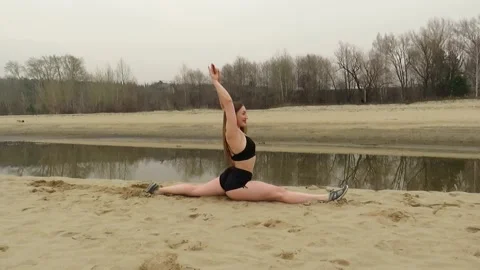 An attractive red-haired woman performs longitudinal splits on the sand Stock Footage 187420899