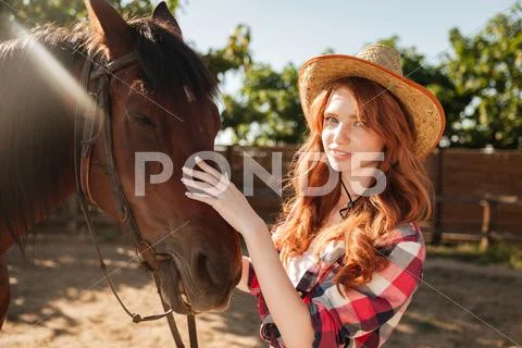 Attractive redhead young woman cowgirl in hat with her horse Stock Photos