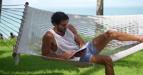 Attractive relaxed dark-haired multi-ethnic bearded man tourist reading a book Stock Footage 221180247