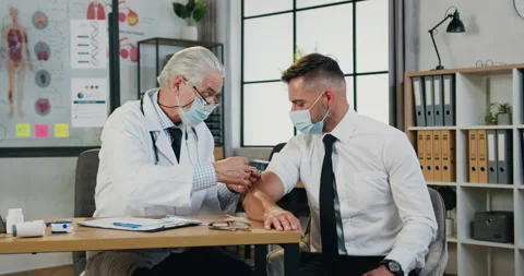 Attractive responsible senior grey-haired male doctor in facemask making vaccine Stock Footage 160839641