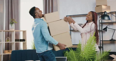 Attractive satisfied young black-skinned man carrying carton boxes into his new Stock Footage 150698973