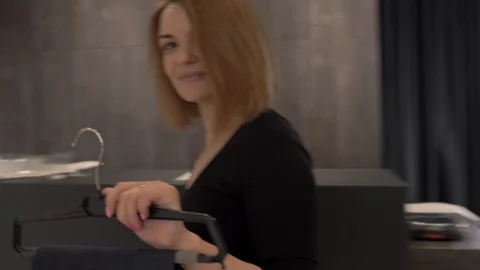 An attractive shop assistant going to a dressing room. Offering trousers to a Stock Footage 107460353