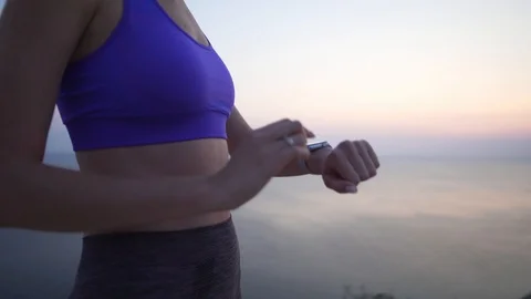 Attractive slim athlete sets up a smart watch before meditation by the ocean Stock Footage 113672016