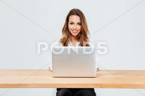 Attractive smiling businesswoman using laptop while sitting at the office Stock Photos