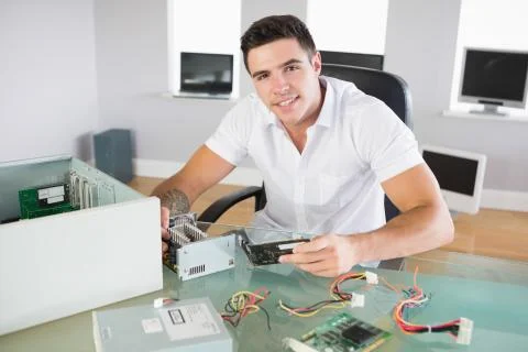 Attractive smiling computer engineer sitting at desk holding hardware Stock Photos