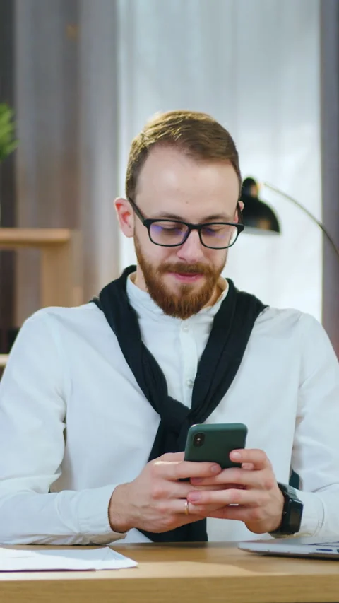 Attractive smiling happy 30-aged bearded office worker writing sms on mobile to  Stock Footage 329494843